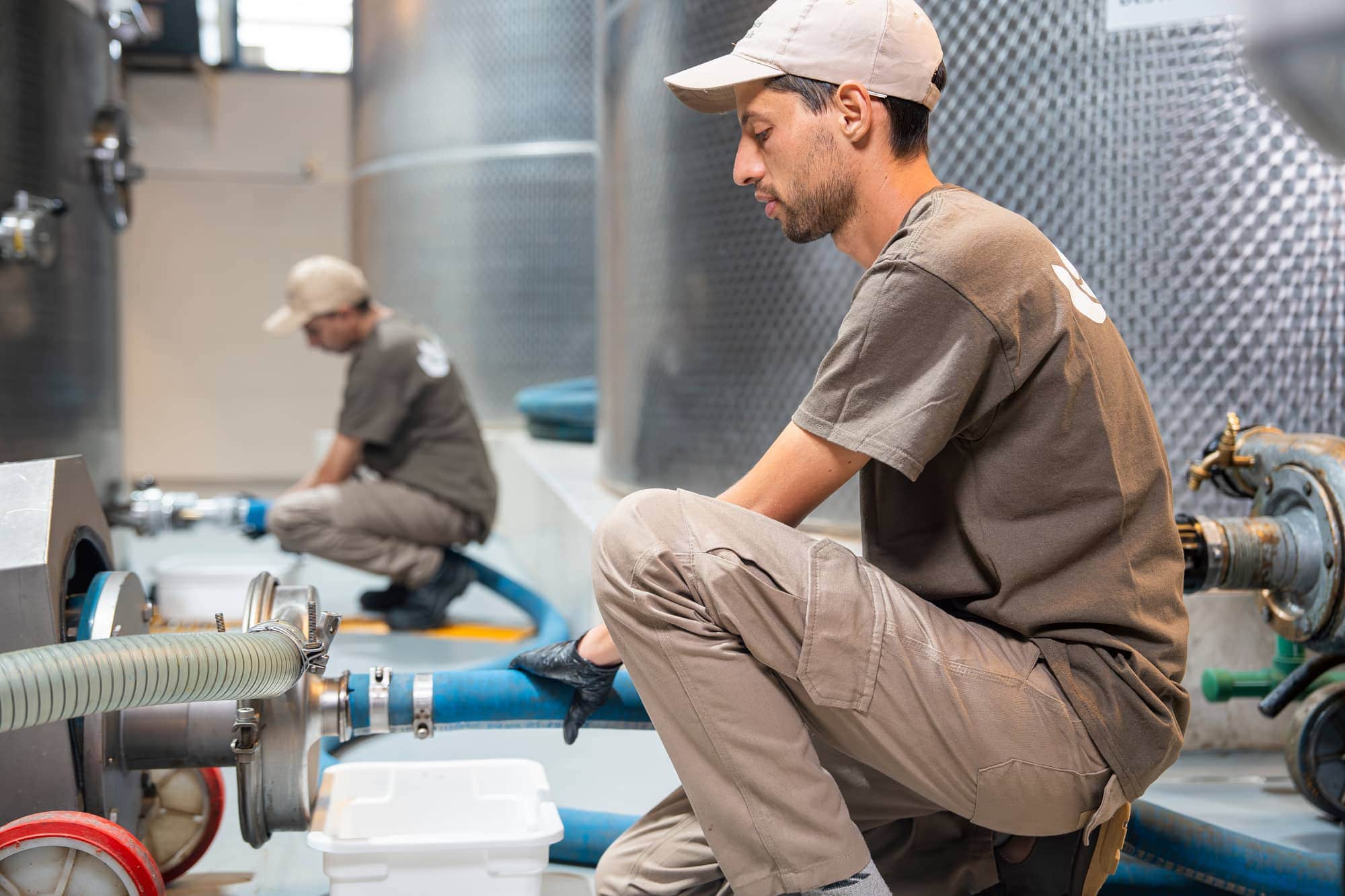 Operadores da Aceites del Valle trabalhando com tanques de aço inoxidável e mangueiras na planta de produção